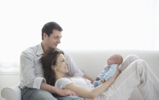 Mom and dad holding baby on a couch. Healthy Foundation for Infant Sleep.