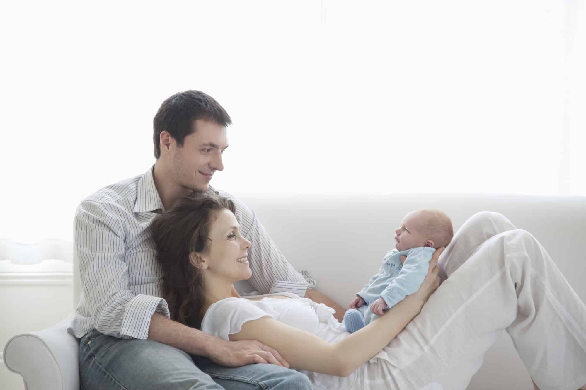 Mom and dad holding baby on a couch. Healthy Foundation for Infant Sleep.